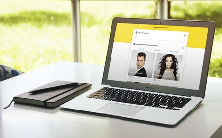 Laptop on a table showing a booking form with hairstyle photos of a man and a woman.
