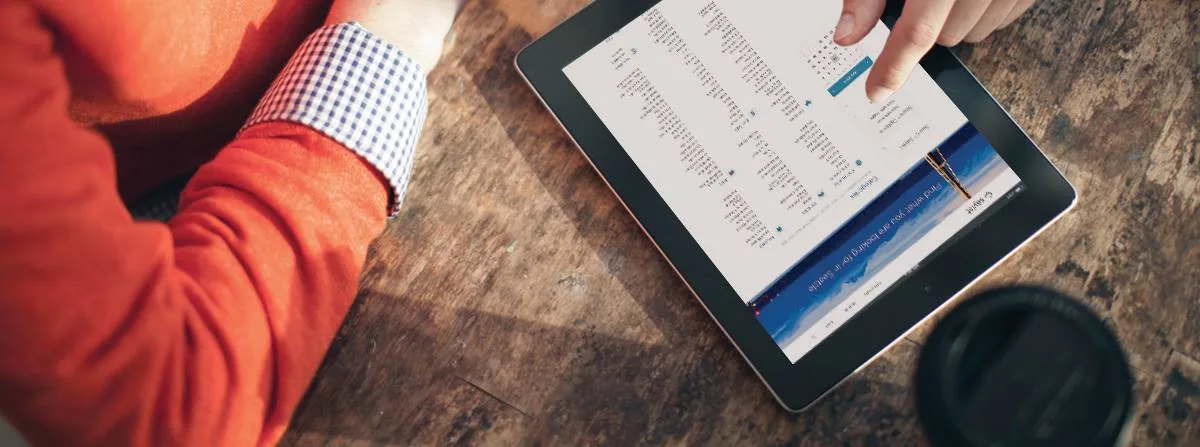 Photo of a hand using a tablet on a wooden table, the site shown upside down on screen.