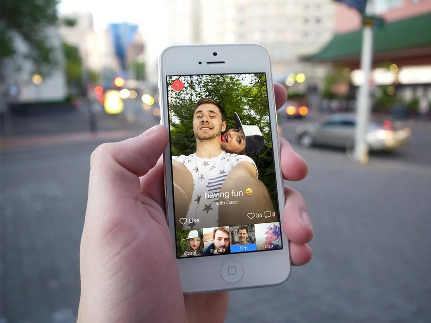 Photo of a hand holding an iPhone showing a man's selfie video with emoji reactions.