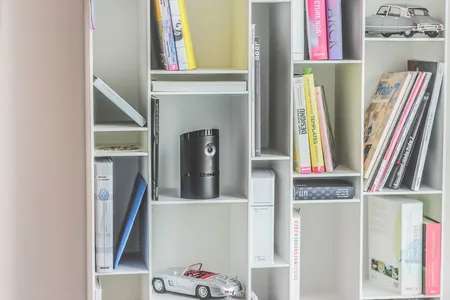 White bookshelf with books, a black cylindrical device and a toy car.