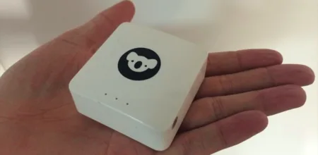 Hand holding a small white device with a koala logo.