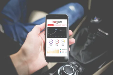Hand holding a phone showing a Hypergrowth analytics dashboard with circular gauges and bar charts.