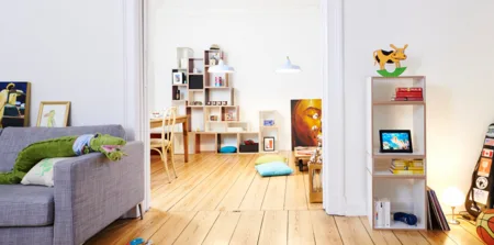 Living room with a grey sofa, a white shelving unit and a wooden floor.