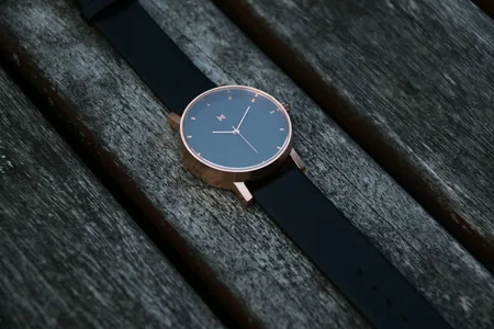 Wristwatch with a black strap lying on a weathered wood surface.